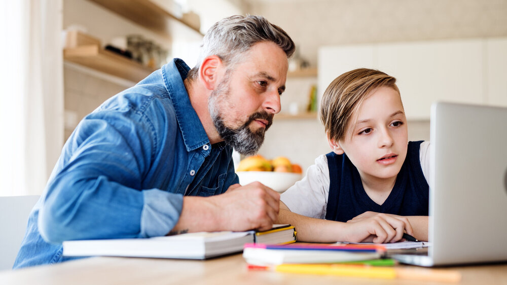 Lehrkraft und Sohn lernen Zuhause gemeinsam mit dem Laptop