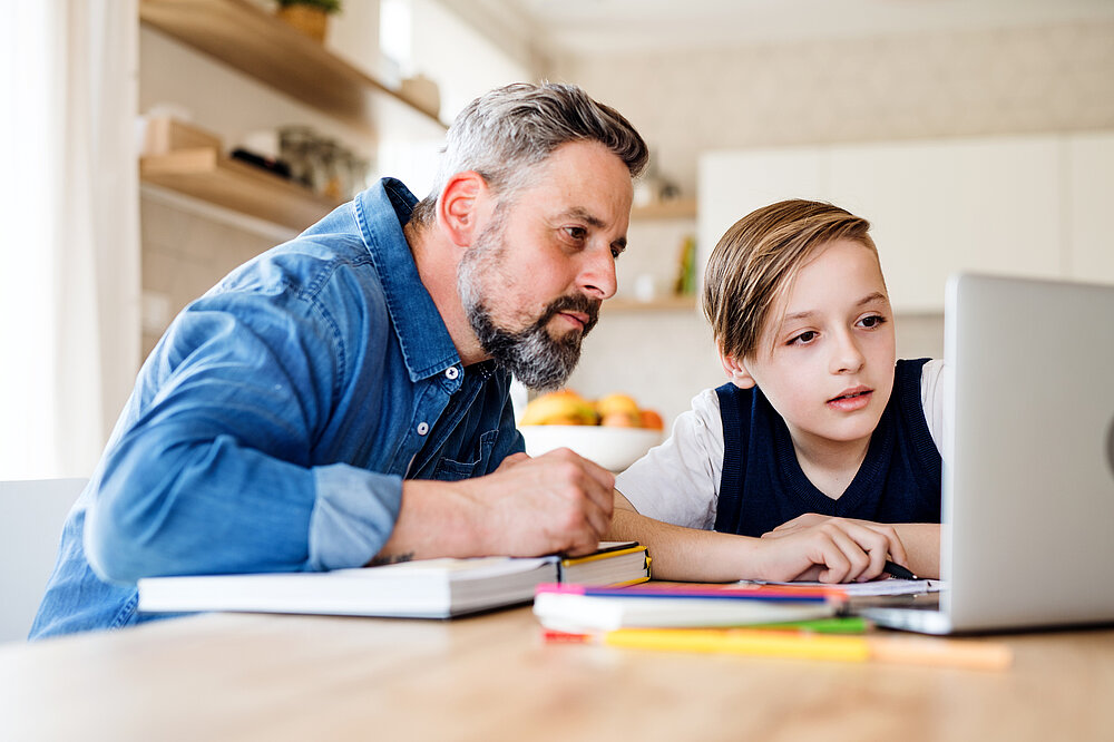 Lehrkraft und Sohn lernen Zuhause gemeinsam mit dem Laptop