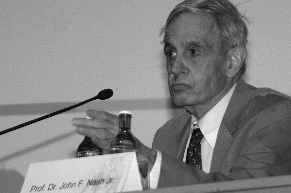 John F. Nash sitzt an einem Tisch mit Mikrofon.